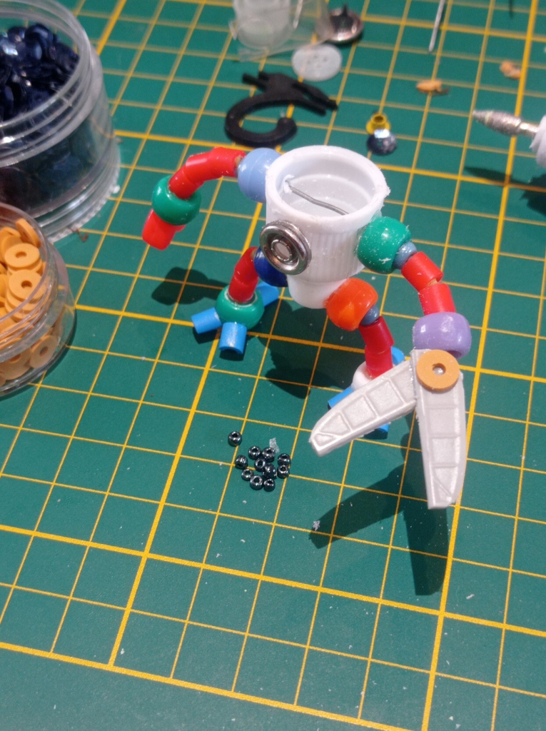 The robot is standing, very small beads are placed at his feet