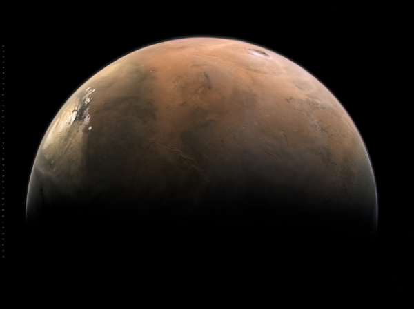 Photograph of Mars taken from space, with a polar ice cap visible on the left and a volcano on the upper right of the image. The lower half of the planet is shrouded in darkness.