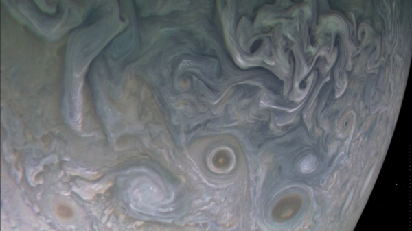 Photograph of Jupiter taken by a passing spacecraft. It is relatively close and only a fraction of the planet is visible. Clouds swirl in massive storms that resemble paint swirling in water.