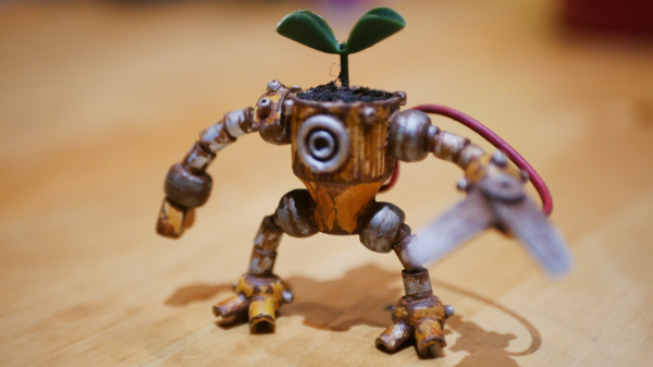 The robot that stands on a wooden table, it has been painted to give a rusty effect. A plant is growing on his head.