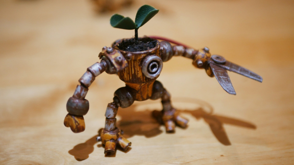 the robot standing on a wooden table, it has been painted to give a rusty effect. A plant is growing on his head