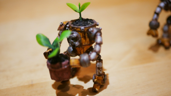 Another robot carrying a flower pot, it has been painted to give a rusty effect. A plant is growing on his head.