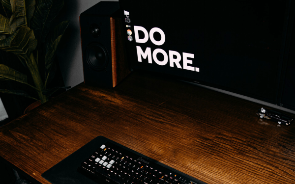 wooden desk with a keyboard, speakers, a toy car, and a monitor with the words "DO MORE" on the screen