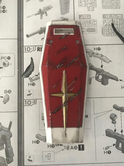 A photo of the Gundam RX-78-2 shield, painted and with battle damage, sitting on the build instructions for the model