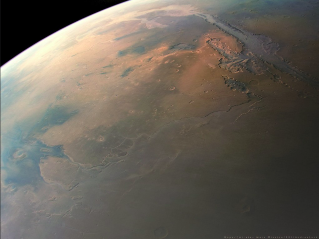 Closer picture of Mars taken from a spacecraft. A giant valley is visible near the top of the picture, in dark grey contrasting with the red tint of the rest of the planet.