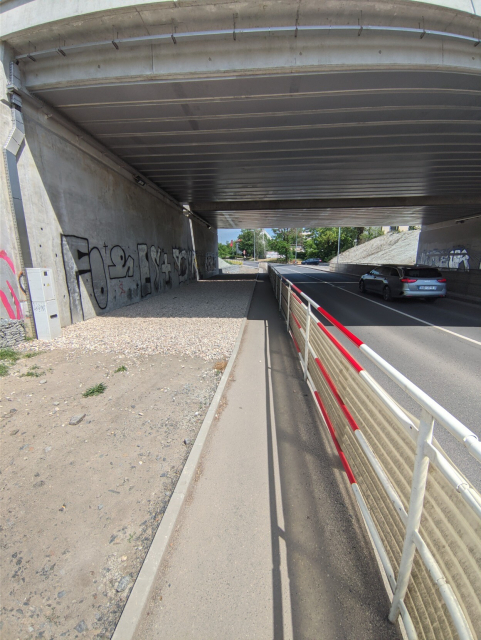 Wide brige over the street. Pavement is narrow, on one side of the pavement there is a fence protecting you form falling to the road, on the other side there is wide useless gravel area.