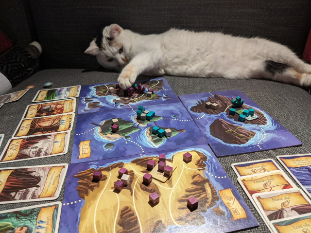 Cat laying next to a board game and reaching the game pieces with her paw.