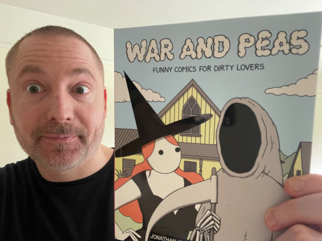 My silly face holding up a small comic book titled War and Peas: funny comics for dirty lovers by Jonathan Kunz and Elizabeth Pich. On the cover is an illustration of a witch with red hair and the grim reaper posing in front of a house.