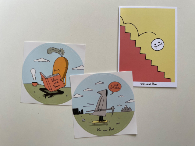 Two circular stickers (one where a carrot with eyes and a mouth is sitting cross-legged, reading a book titled War and Peas as a cup of something hot steams next to it and the other where Death is riding a skateboard while saying “I love my job”) and a small card of a smiley face bouncing down the stairs.