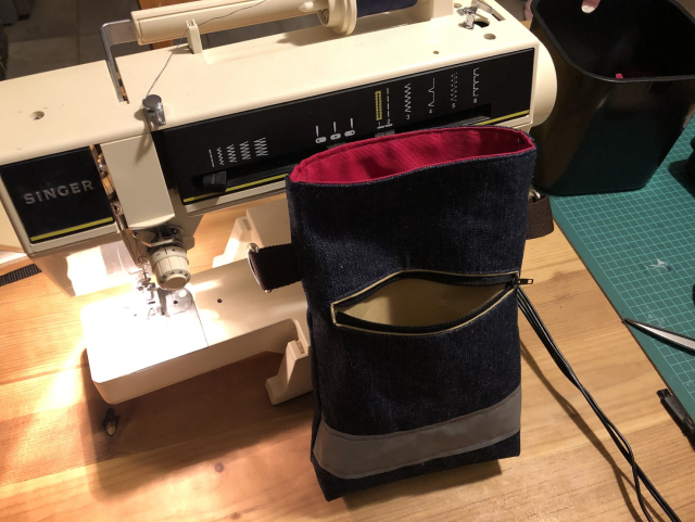 Finished bag resting against a 1990s Singer sewing machine. The bag itself is open, and the pocket too. You can see the pink interior and the beige pocket.