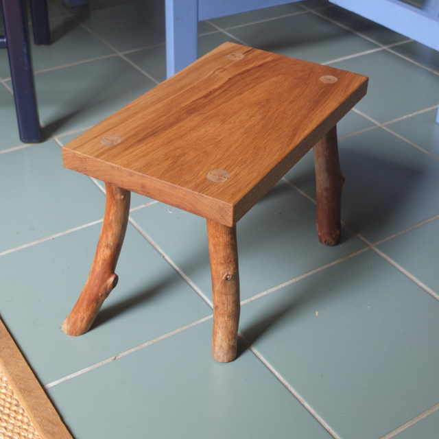 A "milking stool" with four lengths of branches legs. One leg is "stepping" forward. 