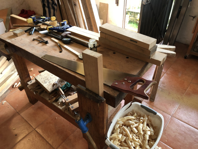 Banco de carpintero con tiras de madera listas para cortar por la mitad. Serrucho largo para corte longitudinal. Un basurero lleno de viruta.