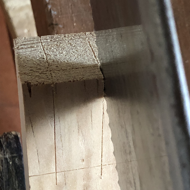 Serruchando a la derecha de la línea marcada. Se serrucha en dos planos (sobre la cara de la tira de madera y sobre el extremo), para que esas dos líneas que se intersectan en el espacio determinen el plano de la hoja del serrucho.