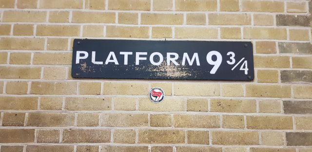 Sticker with the antifa logo and "anti-harry potter aktion: read another book" at the sign for Platform 9 3/4 at King's Cross Station
