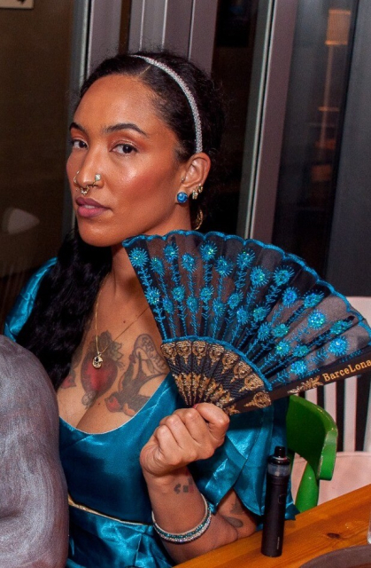 a brown femme wearing a regency gown and holding a fan