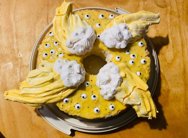 Top view of a ring shaped angel food cake with yellow kiwi-lemon curd, candy eyes, and white and yellow meringue wings on top