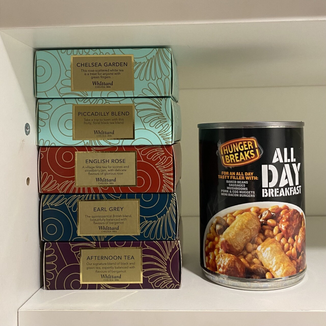 Cupboard shelf with boxes of very fancy tea bags and a tin of All Day Breakfast.