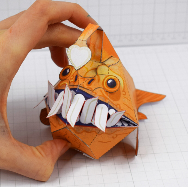 A papercraft of a stylised anglerfish, with its mouth closed, teeth intertwined 