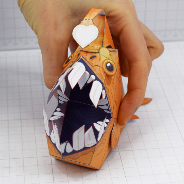 A papercraft of a stylised anglerfish, with its mouth open, a large dark maw agape 