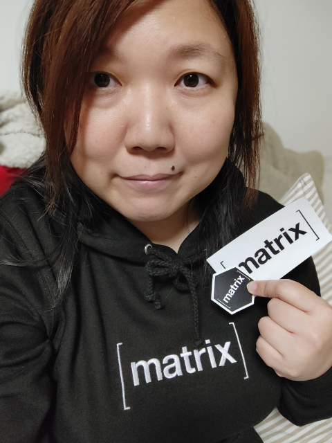 Selfie wearing a black hoodie with [matrix] in white across the front of the hoodie. Holding a couple of matrix stickers in my left hand.