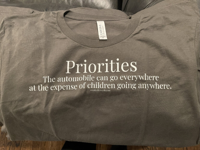 A T-shirt that says: Priorities: the automobile can go everywhere at the expense of children going anywhere.