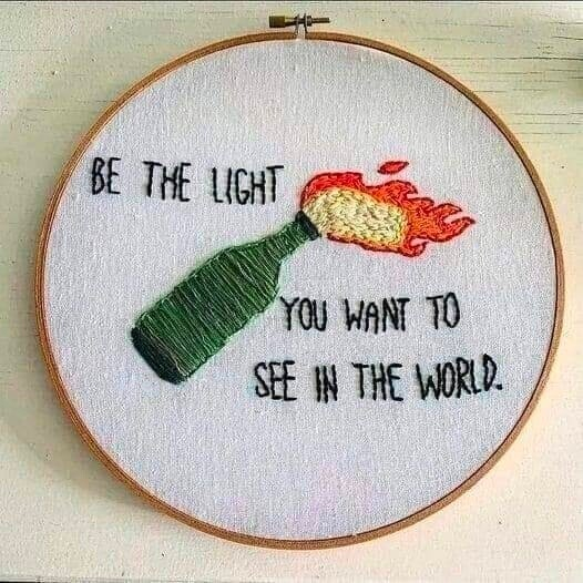 A stiched and lit molotov cocktail flying. text: 'BE THE LIGHT YOU WANT TO SEE IN THE WORLD'.