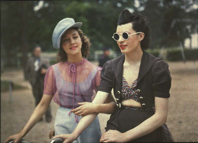 very early color photography picturing two young women in a Paris public garden.  they are casually arms in arms, as if in conversation, and they are dressed in suprisingly modern fashion.