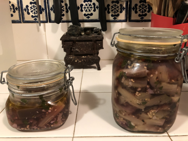 Dos frascos de berenjenas en escabeche, uno chico a medio comer, y uno grande en fermentación.