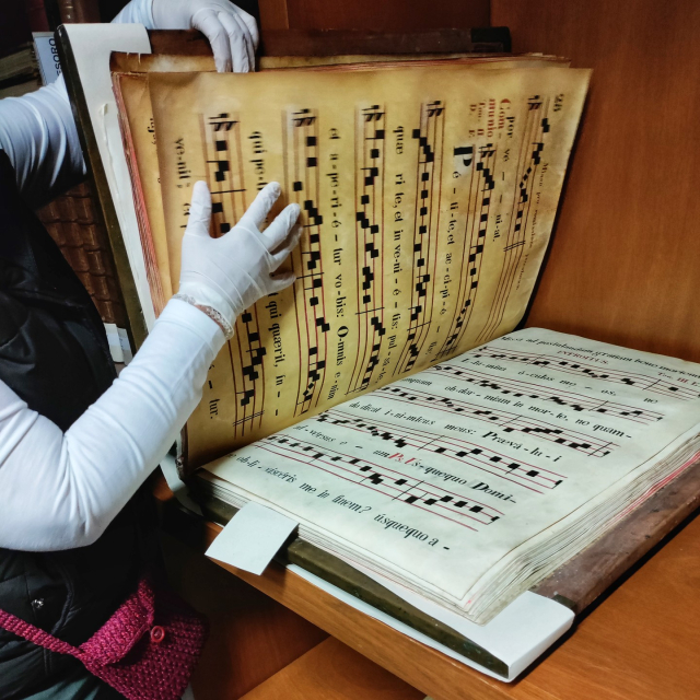 Las manos enguantadas de una especialista abren un libro antiguo con partituras corales.