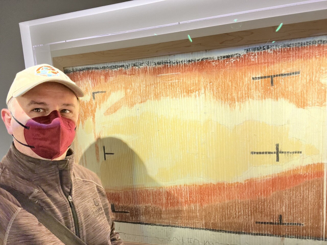 Me, Dr. Fred J. Calef III, wearing a baseball cap, red N95 mask, and brown/black jacket, standing in front of the pastel Mariner map. It was hand colored from numbers printed in vertical strips of paper in yellow, orange, and brown pastels.
