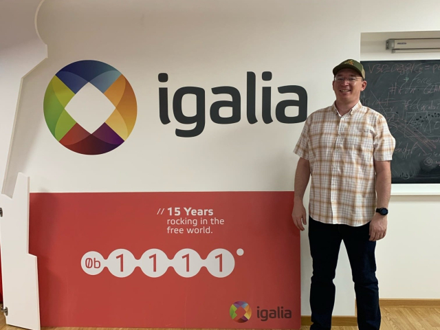 Rob in front of a sign that says "Igalia, 15 years rocking in the free world"