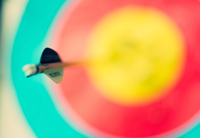 A photograph of an arrow that has hit the center of its target, rendered colorfully with only the arrow's fletching in focus.