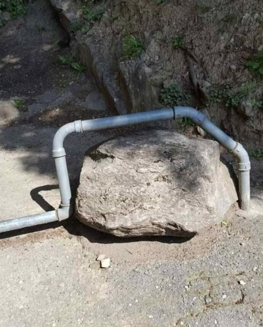 A picture outdoor with a pipe going over and around a boulder in an awkward way. The boulder was clearly in the way, but not removed.
