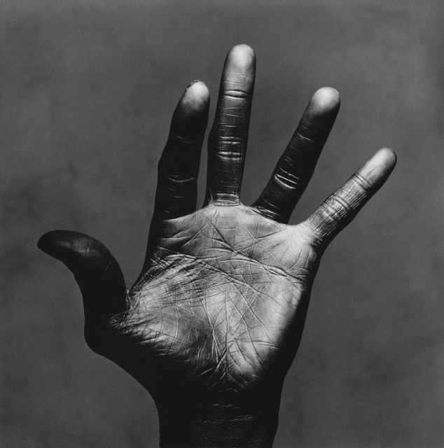Black and White photo of Miles Davis' left hand against a murky gray background, thumb hooked back, little finger splayed, middle fingers looking as if they are forming a musical phrase on fingering a horn