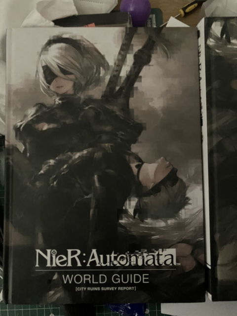 The cover of the first volume of the Nier:Automata World Guide, showing 2B holding 9S in her arms