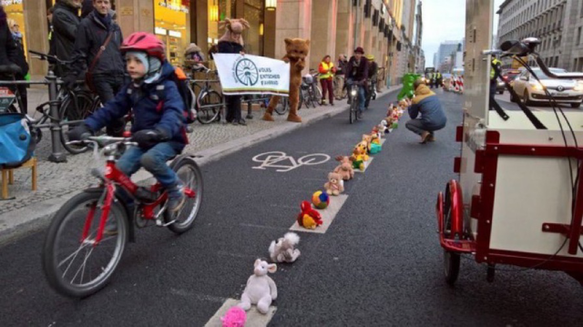 Kids riding bikes in bike-lanes defined by a row of stuffed animals in Berlin, Germany