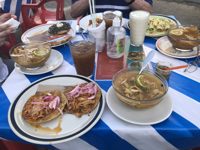 Tazón repleto de sopa de lima (tortilla frita, pollo, lima) y plato con panuchos de cochinita pibil.