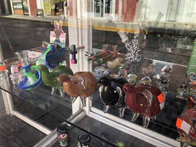 Pipas de vidrio en forma de elefante, en un aparador con pipas de otras formas.
