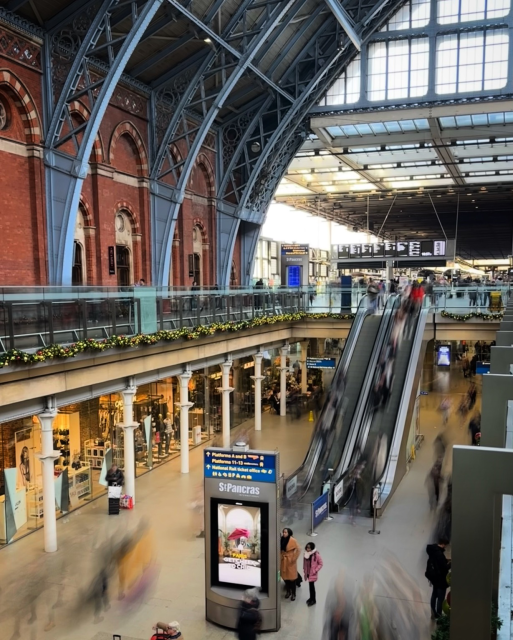St. Pancras’s station from the upper level with blurred outlines of people going down the escalator and under the great arch. 
