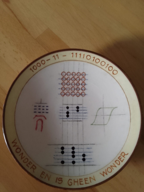 A plate with five mysterious pictures. On the rim, these the date 8-3-1956 in binary, and the text Wonder en is gheen wonder.