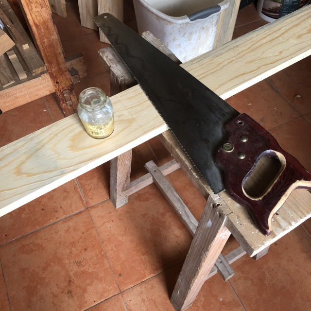 Tabla puesta sobre el burrito de serruchar; serrucho de corte transversal, frasquito con grasa lubricante.
