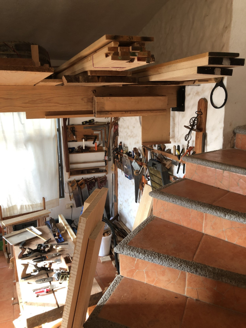 Workshop with a somewhat tall ceiling. Two beams support a bunch of wood while its moisture reaches equilibrium.