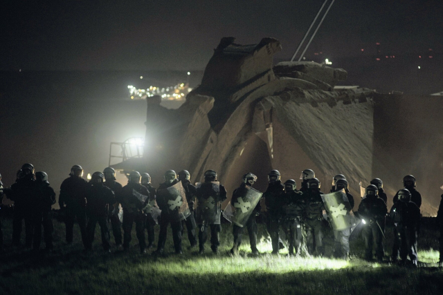 Many police officers stand infront of a coal excavator
