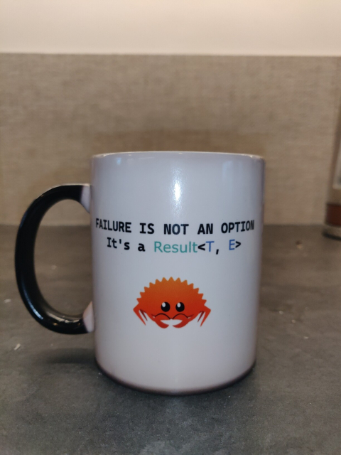 A cup showing Ferris, the Rust language mascot, and the text: failure is not an Option, it is a Result<T, E>
