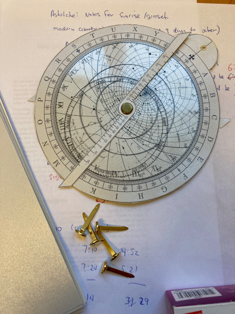 A handmade astrolabe made from card-stock and transparency sits on a table on some notes for doing calculations with the astrolabe and material for building new ones.

The picture is the of the front of the astrolabe and you can see the clear piece with constellations overlaying the background of the sky elevation markings with time and elevation scales on the outer rim.
