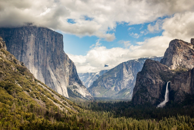 Picture of the tunnel view, showing El Capitan, a cloudy half dome and a full Bridalveil falls under a blue cloudy sky.