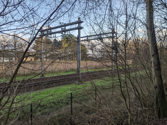 Snímek úseku železniční tratě Roosendaal - Essen.  Na snímku jsou dvě brány nesoucí trolejové vedení. Trolejové vedení nizozemského systému 1500 V DC končí na bližší bráně, na vzdálenější bráně začíná trolejové vedení belgického systému 3000 V DC. Mezi branami není žádné vedení.