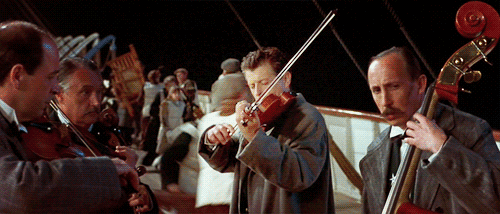 four men in the foreground playing as part of a string quartet, as part of a scene from the movie Titanic, where the quartet kept playing as the ship sank.