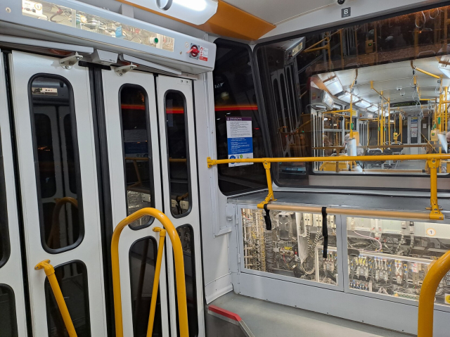 Photo of the inside of a tram car, with see-through panels set into the back wall and above the doors, showing numbered mechanical and electronic parts.