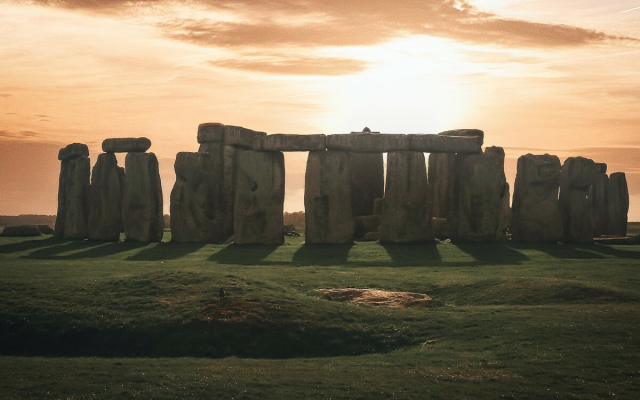 Picture of a sunset across the stones of the famous Stonehenge in the UK during the months from spring to autumn where the ground is green. 